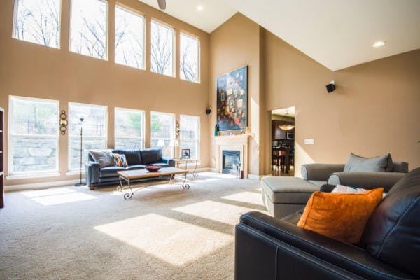 A livingroom with high vaulted ceilings, full of windows on the tallest wall, allowing plenty of sunlight coming in.