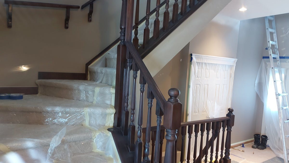 interior painting - Stained brown railing being prepared for painting. Carpet Steps are being protected with a special plastic